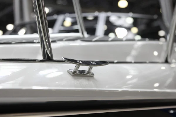 Stainless steel flush deck cleat on the white gelcoat gunwale of a boat, shown in a showroom setting.