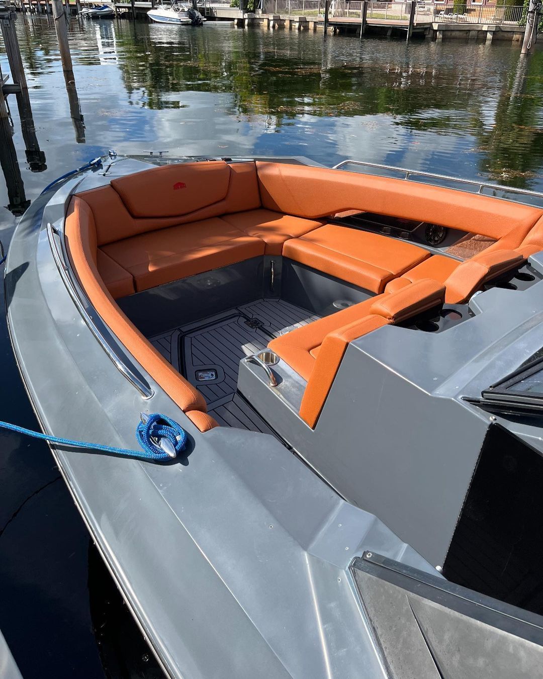 Orange upholstered U-shaped lounge seating on a gray powerboat moored at a residential canal dock.