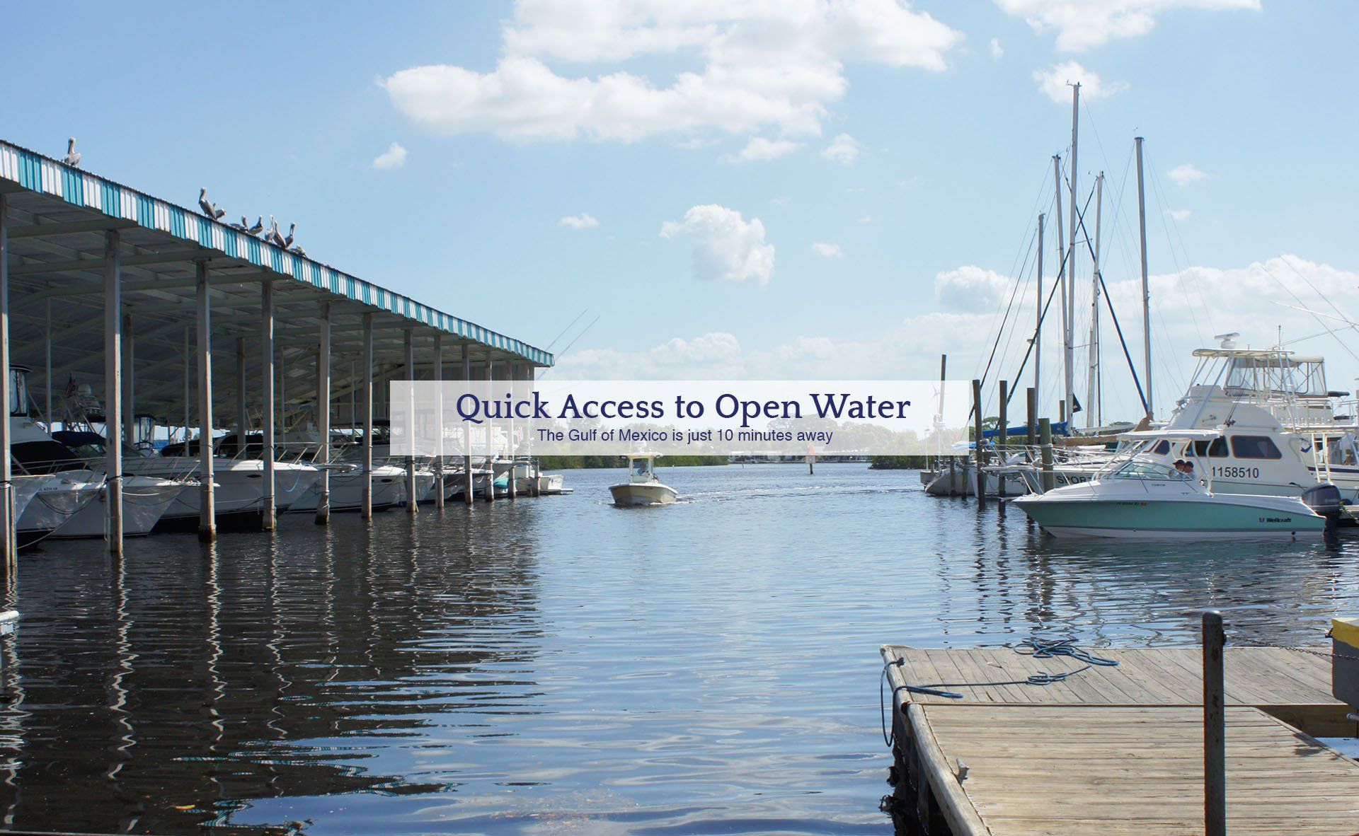 Covered boat slips and a waterway channel with motorboats and sailboats at a marina, with pelicans perched on the roof.