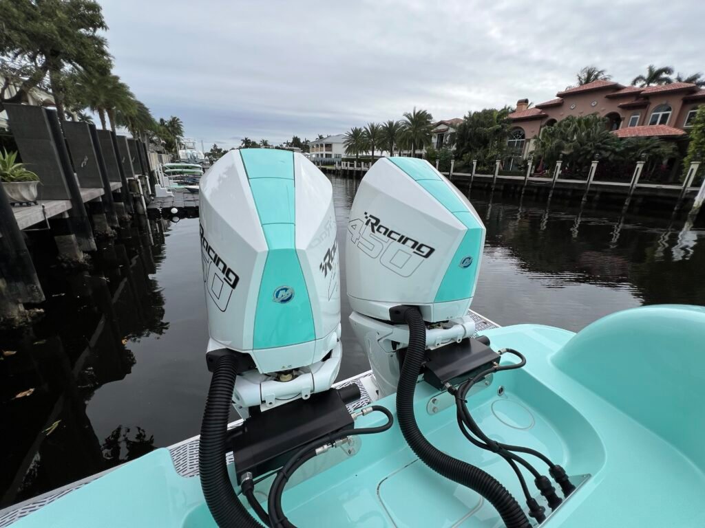 Twin Mercury Racing 450 outboard engines mounted on a teal boat in a residential canal with palm trees and Spanish-style homes.