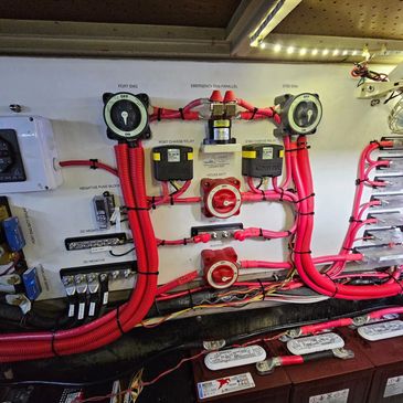 Marine electrical distribution panel with red battery selector switches and wiring loom on a boat's bulkhead.