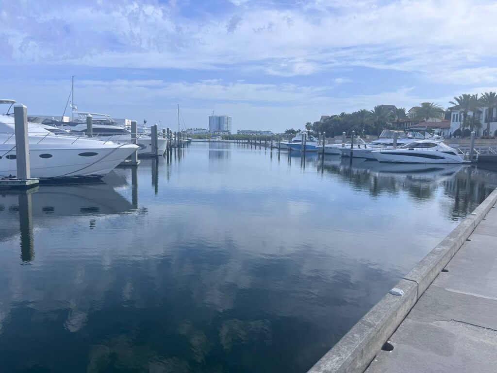 Calm marina basin lined with white motor yachts moored at docks under a partly cloudy sky.