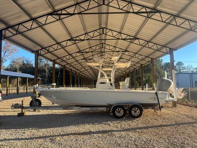 White center-console fishing boat on a trailer under a covered metal storage shed with gravel ground.