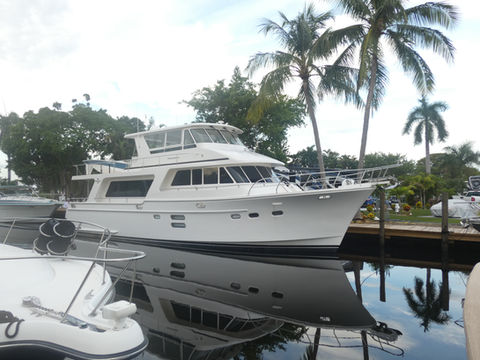 White motor yacht moored at a canal dock lined with palm trees, with a smaller tender boat in the foreground.