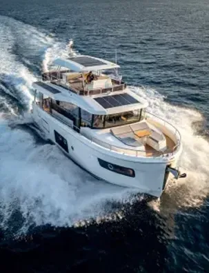 White motor yacht with solar panels cruising at speed, leaving a white wake across open water.