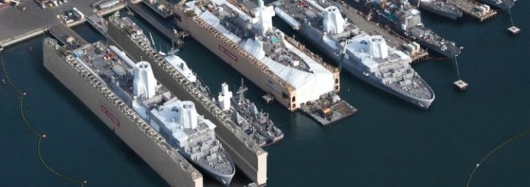 Aerial view of naval amphibious ships in dry docks and berthed at a shipyard harbor.