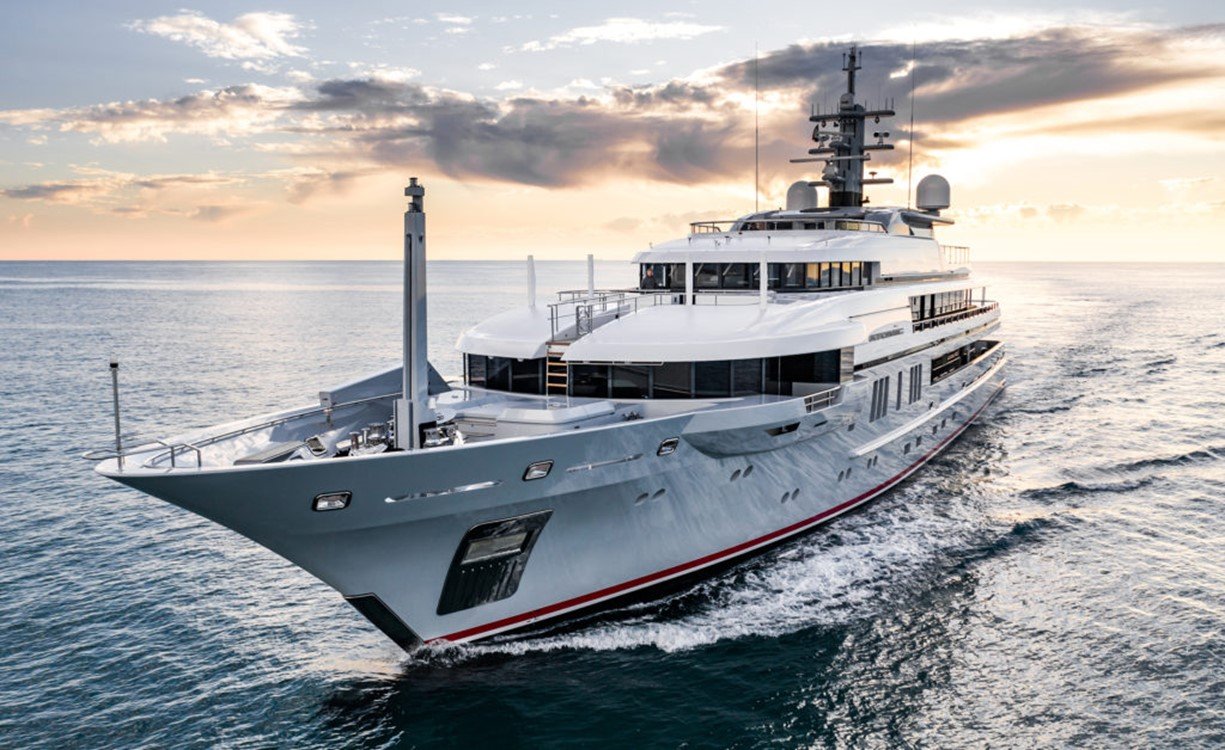 Large white motor yacht underway on open water at sunset, with its radar mast and exhaust funnel visible.