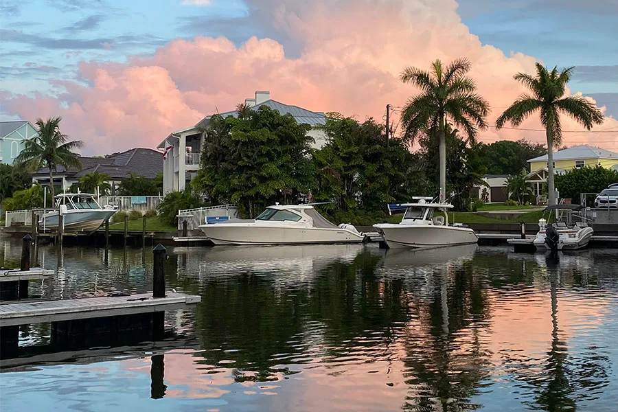 Two white motorboats moored at a canal-side dock with palm trees and waterfront homes at sunset.