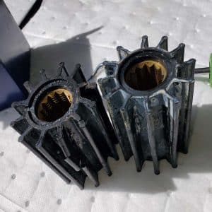 Two black rubber marine water pump impellers, one larger than the other, lying on a white surface.