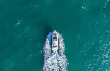 Aerial view of a white motor yacht cruising through turquoise water with a trailing white wake.