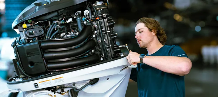 Technician servicing an outboard motor on a boat in a workshop.