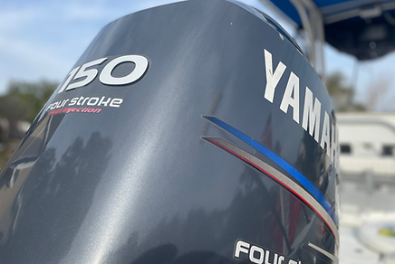 Yamaha 150 four-stroke outboard motor mounted on a boat with blue sky and trees in the background.