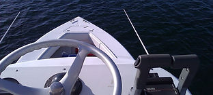 Boat bow and steering wheel viewed from the helm over calm blue water.