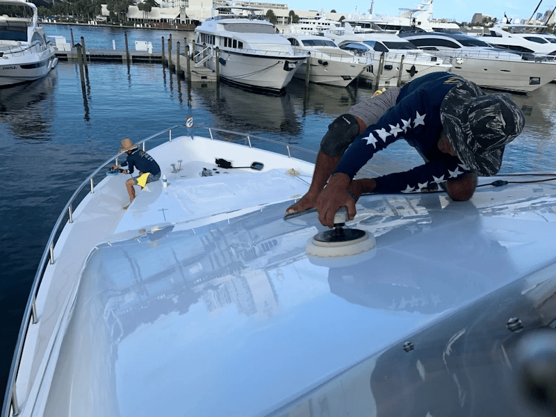 Crew polishing the white fiberglass deck of a motor yacht at a marina dock.