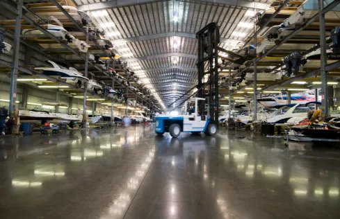 Forklift moving through an indoor boat storage facility with boats stacked on racks along both sides.