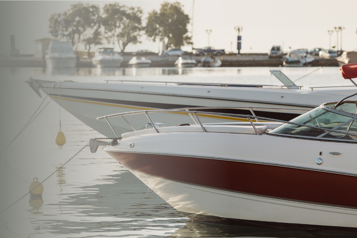 Two white motorboats moored side by side at a marina with fenders and mooring lines, with parked cars and trees visible in the background.