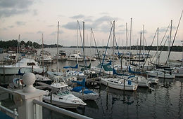 Sailboats and powerboats moored in rows at a marina at dusk, with a white railing in the foreground.