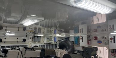 Engine room interior of a vessel showing electrical control panels, gauges and machinery under overhead lighting.
