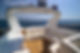 Blurred view of a boat deck with a white structure over calm water under a blue sky.