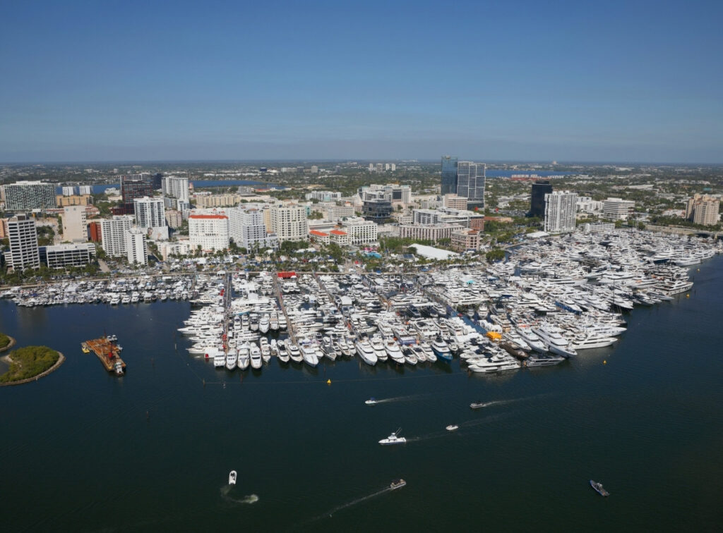 Aerial view of a crowded yacht show with hundreds of superyachts moored along the waterfront of a coastal city.