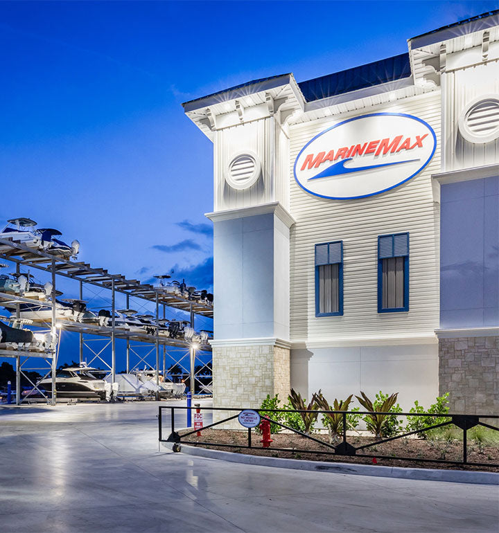 Exterior of the MarineMax dealership with boats stored on multi-tier racks and a sport yacht in the lot at dusk.