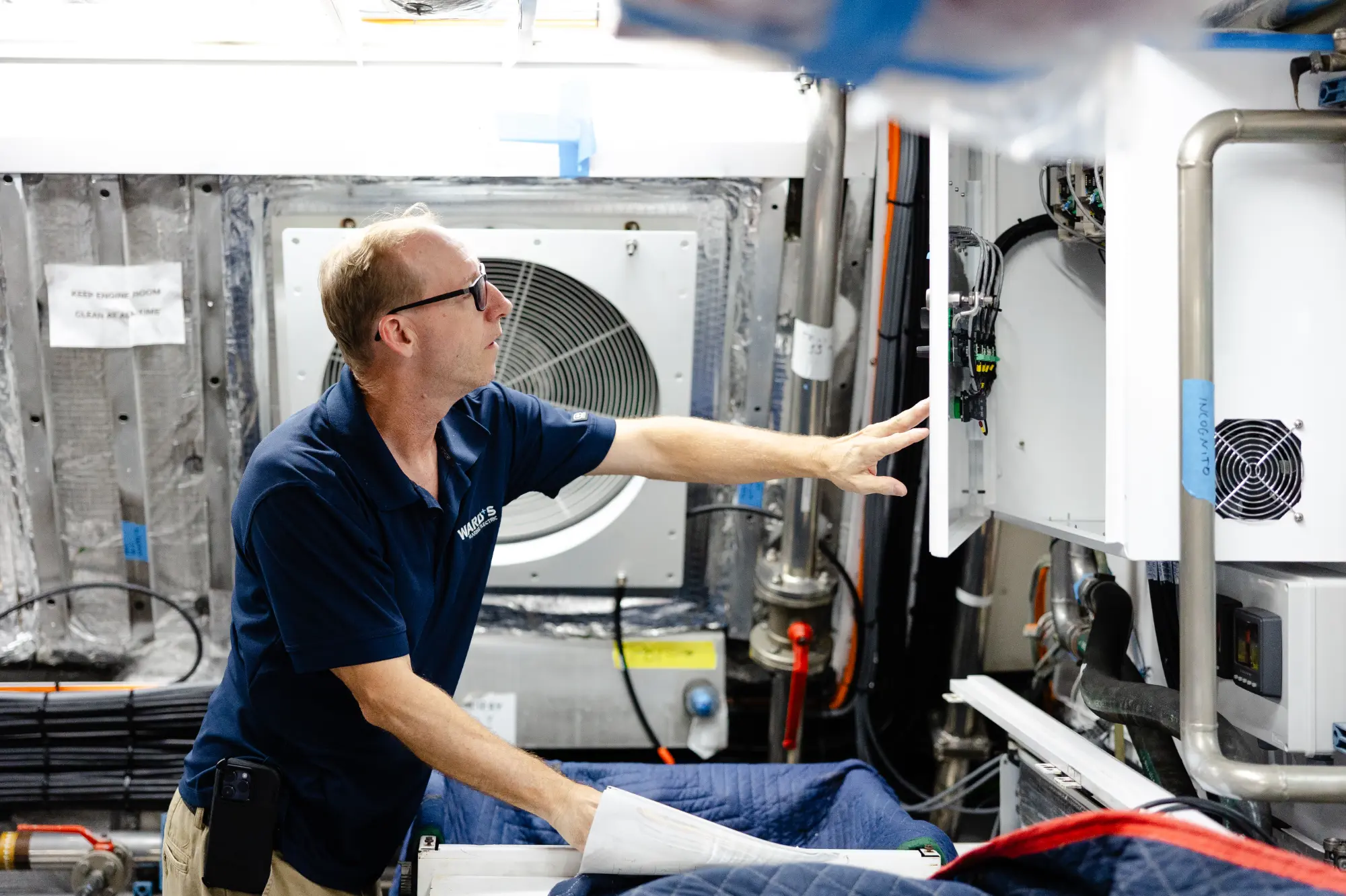 Technician inspecting an electrical control panel in a boat engine room at Ward's Marine Electric.
