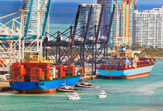 Container ships docked at a cargo terminal with gantry cranes and tugboats, Miami
