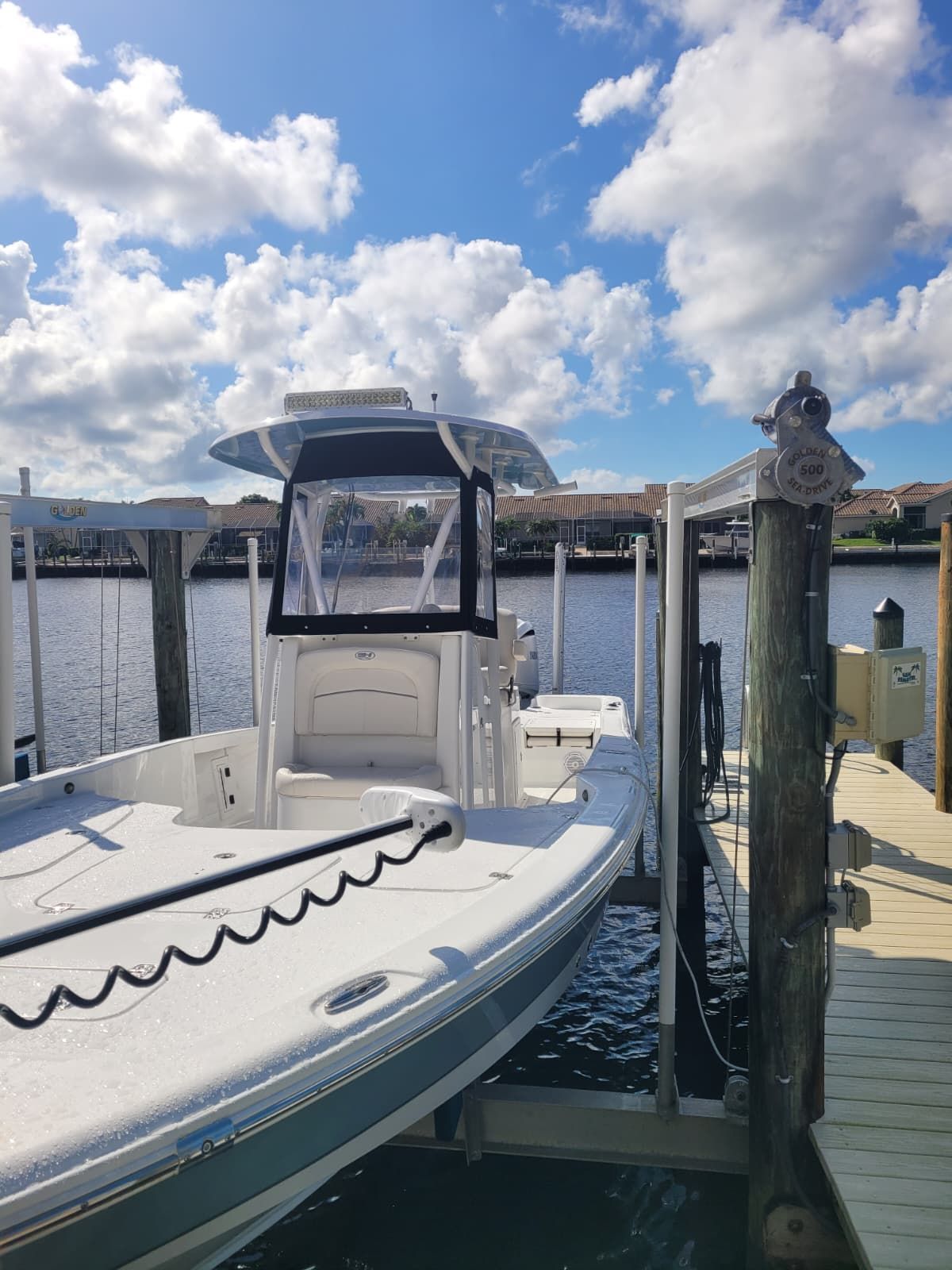 White center console boat with a black canvas enclosure and T-top sitting in a Golden Sea-Drive boat lift at a canal dock.