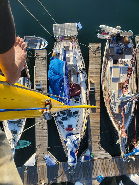 Overhead view of sailboats tied up at a wooden dock, with a yellow sail boom in the foreground.