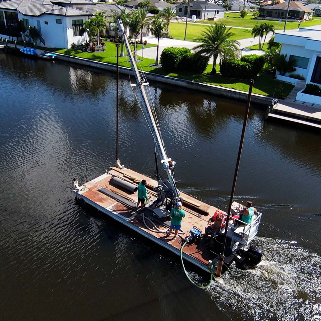Work barge with a crane and crew operating on a residential canal with waterfront homes, Cape Coral.