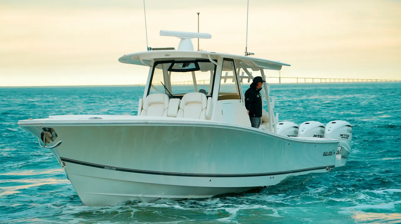 White center-console sportfishing boat with three Yamaha XTO outboards underway on turquoise water at sunset, with a person standing at the helm.