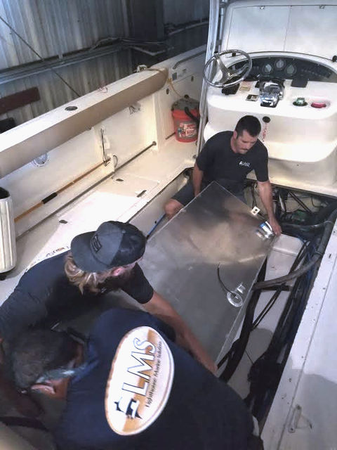 Three technicians lifting a metal panel from a boat's cockpit deck at Lighthouse Marine Solutions.
