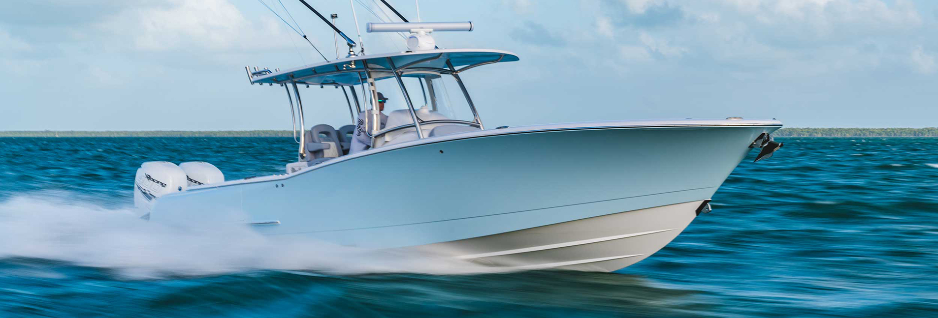 White center console sport fishing boat with twin outboard engines and a T-top running fast across open blue water.
