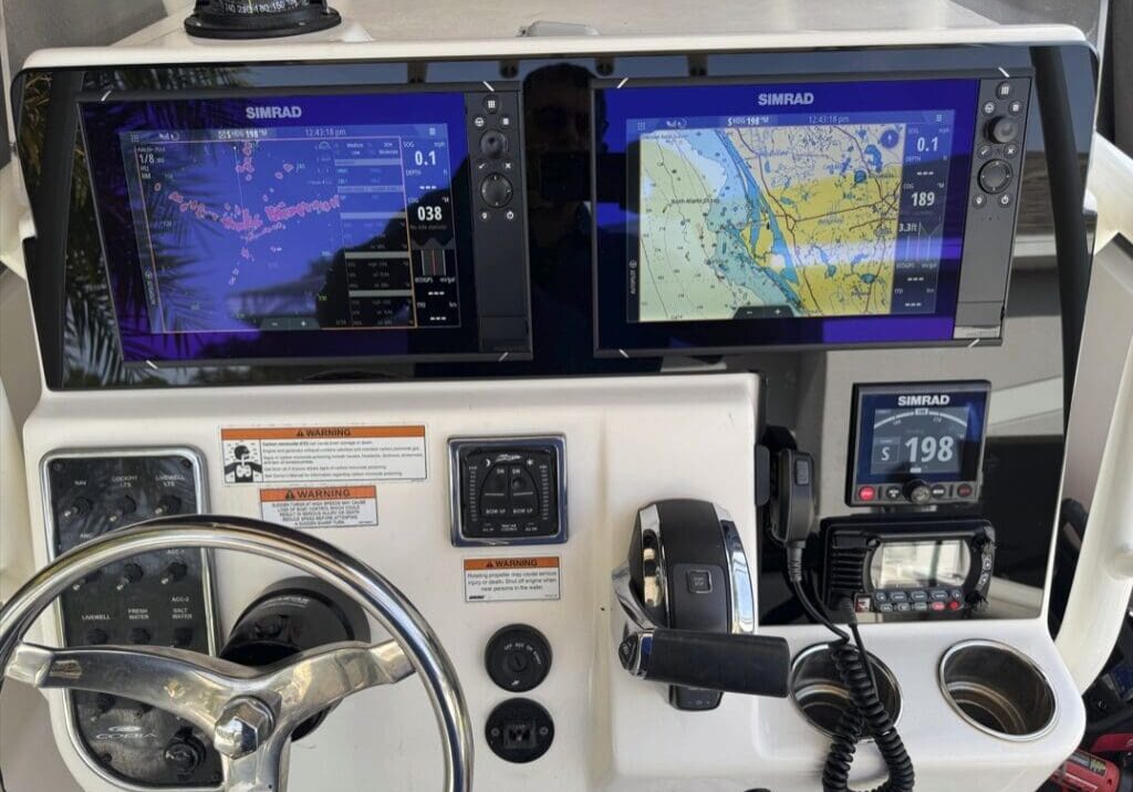 Boat helm station with twin Simrad chartplotter displays, VHF radio and engine controls on a white center console.