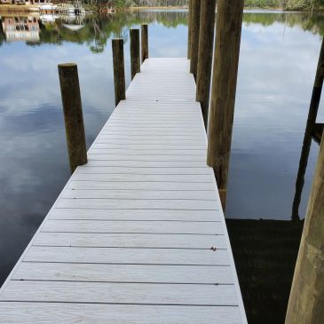 White composite dock walkway extending over calm water on wooden pilings.