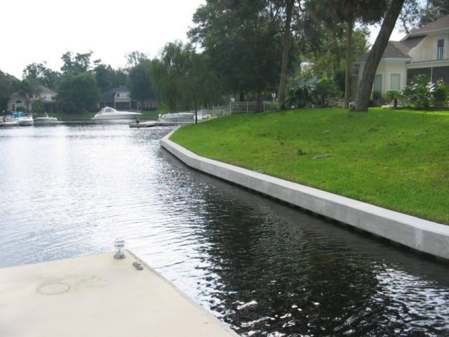 Newly built concrete seawall and boat dock along a residential canal lined with lawns and homes.