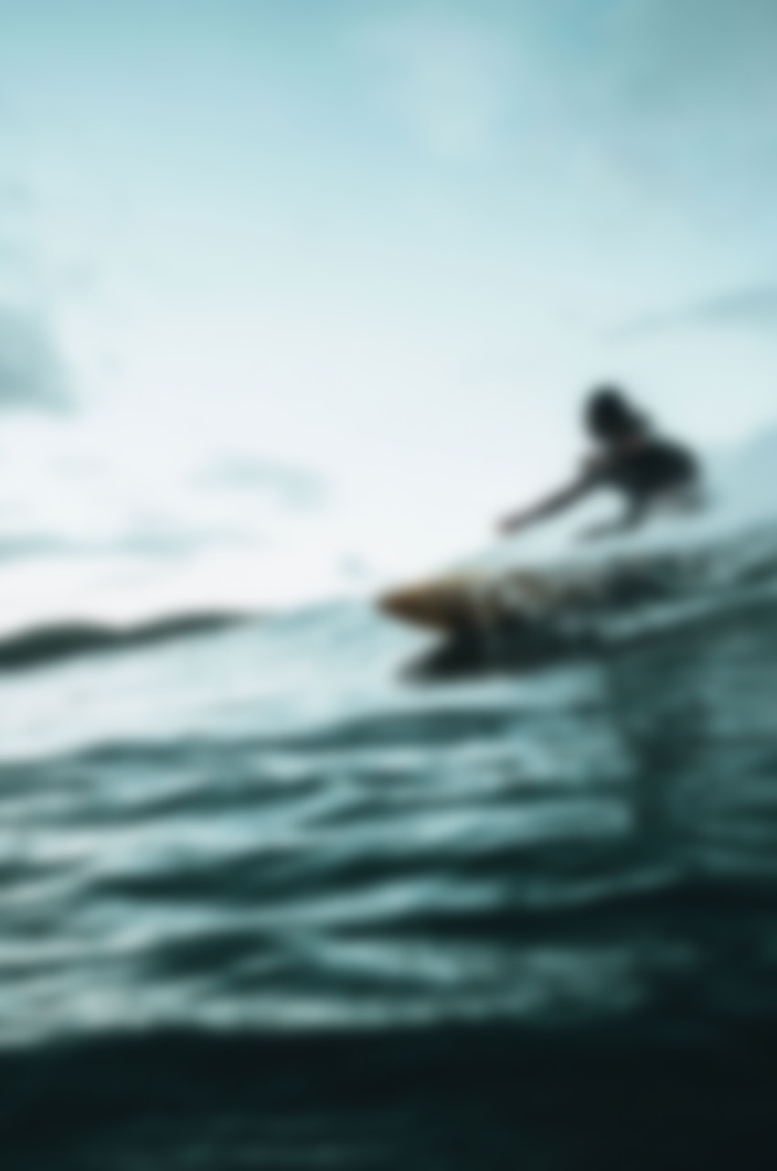 Blurred surfer riding a wave on a surfboard in open ocean water.