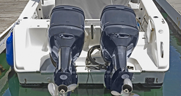 Twin outboard motors mounted on the transom of a white boat at a dock.