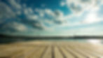 Wooden deck boards extending toward a calm bay under a partly cloudy sky.