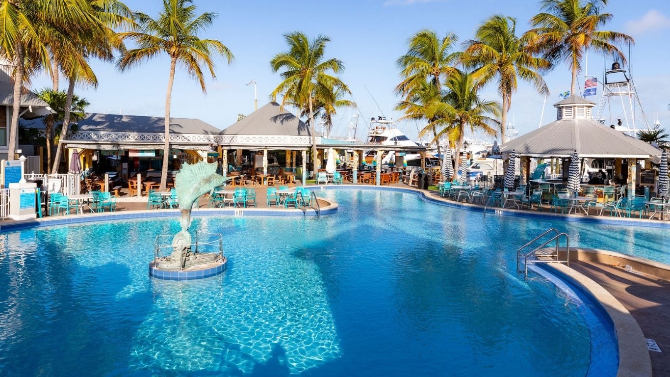 Pool with a bronze sailfish fountain and palm-lined deck at a waterfront resort marina, with yachts moored nearby.