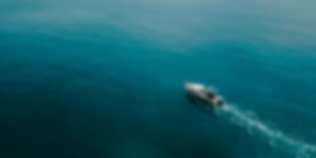 Small motorboat leaving a white wake across open blue water, seen from above.
