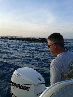 Man steering a boat with an Evinrude outboard motor on open water near a rocky breakwater.