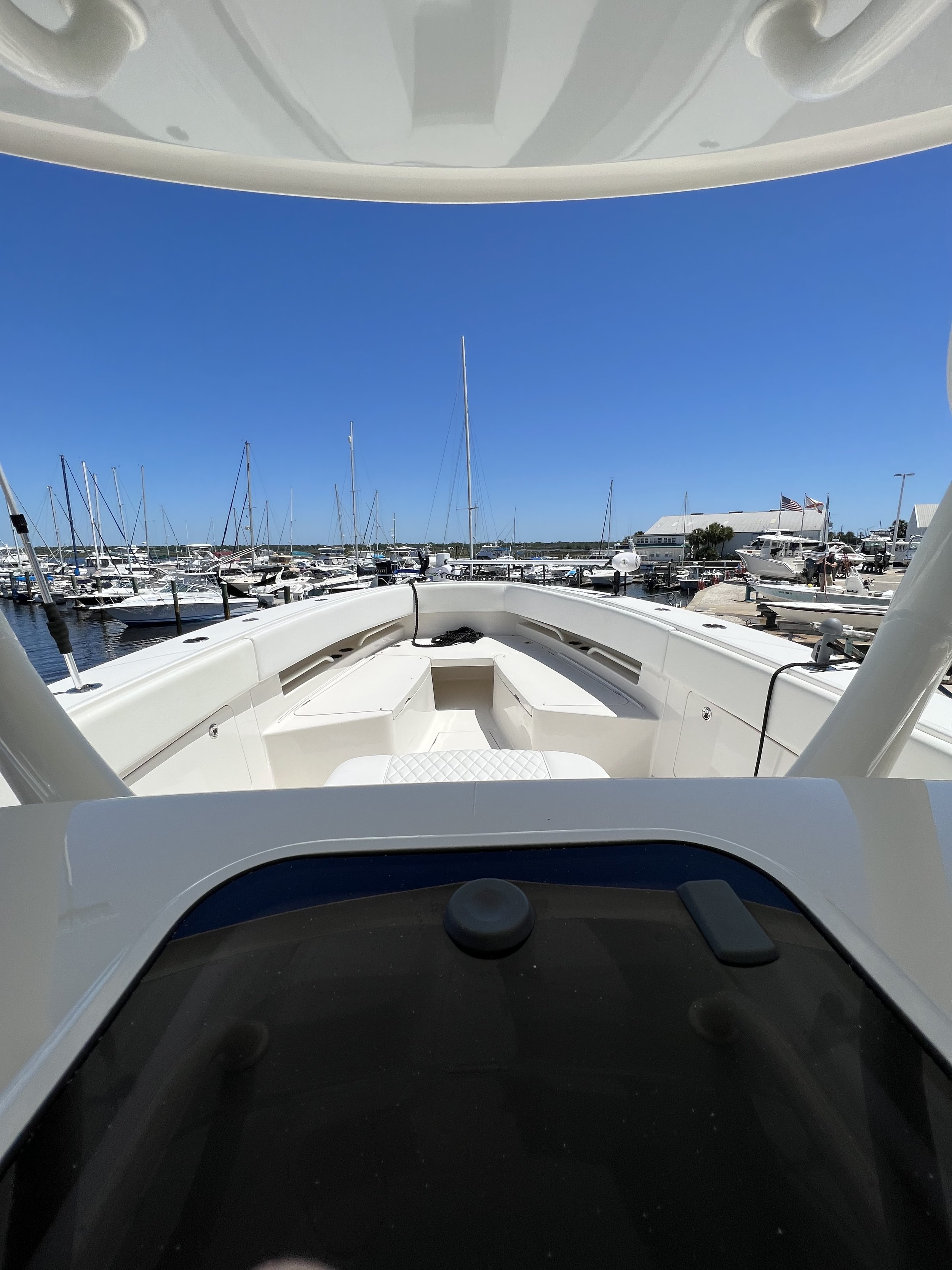 View from the helm of a white center console boat over the bow seating and a busy marina with docked sailboats and powerboats.