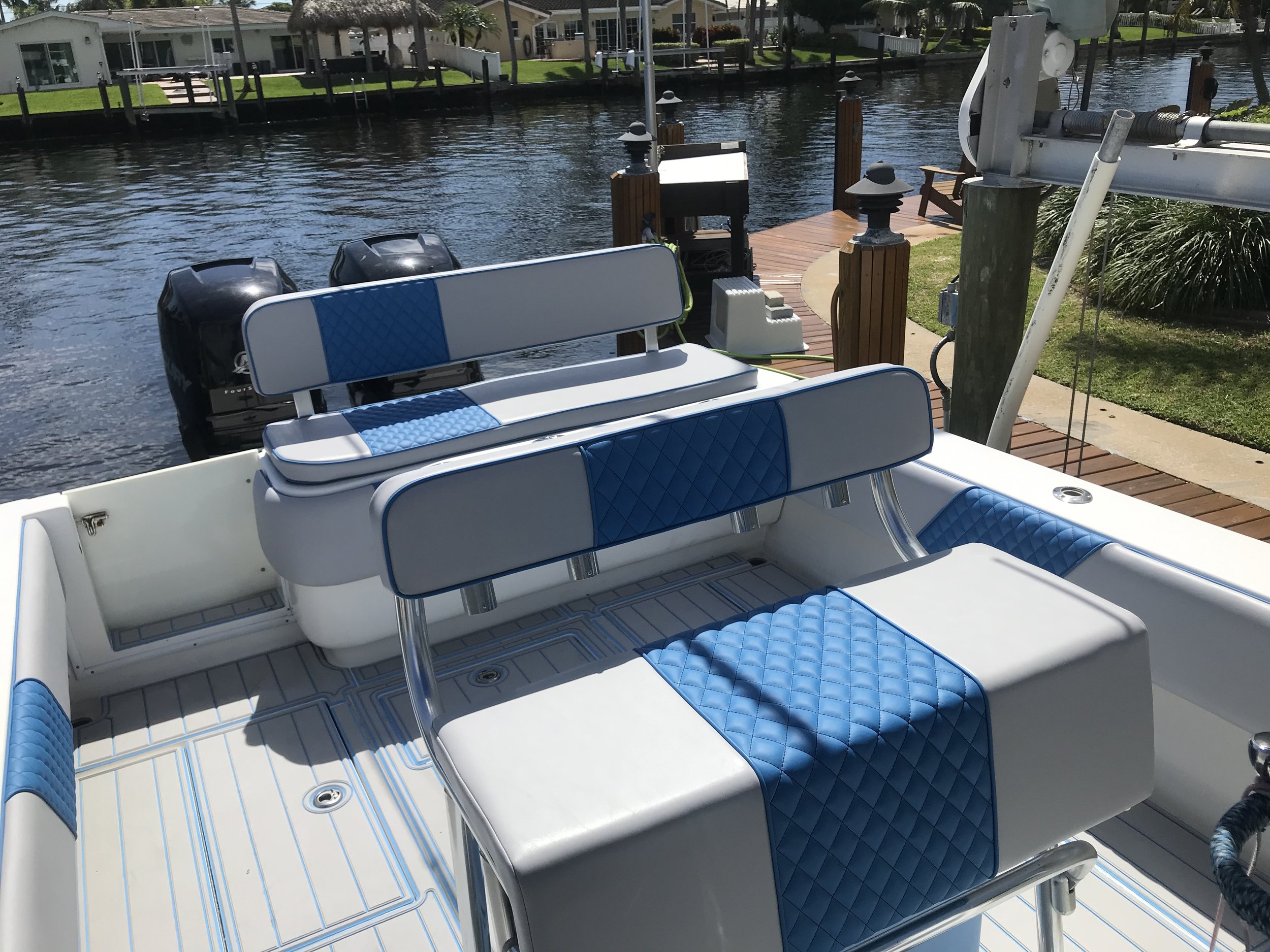 Blue and white quilted helm and bench seating with a non-slip deck on a boat at a dock on a canal, with outboard motors visible behind the seats.