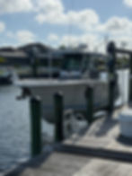 White boat moored at a wooden dock with green pilings in a marina.