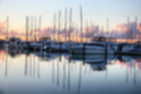 Sailboat masts and motor boats moored at a marina dock at dusk with reflections on the water.