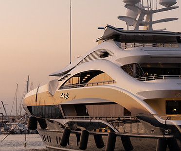 Luxury motor yacht moored at a marina at dusk, with fenders along the hull and sailboat masts in the background.