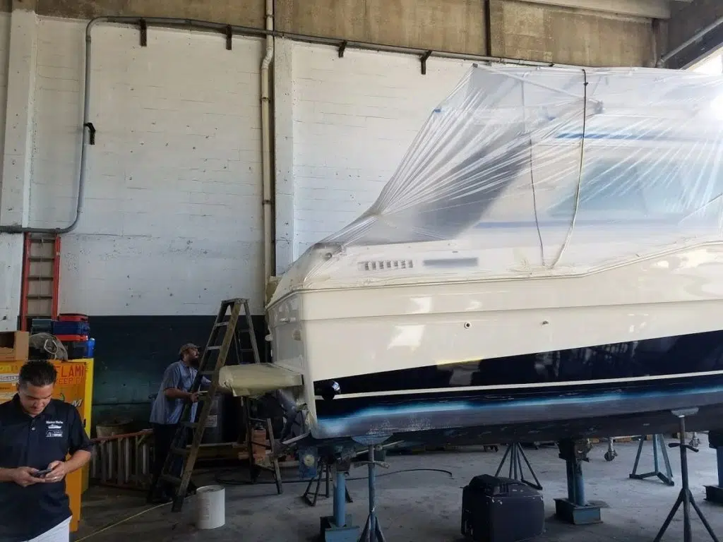 Cream and navy motor yacht on stands wrapped in plastic at Masters Marine, Dania Beach while crew works on the hull.