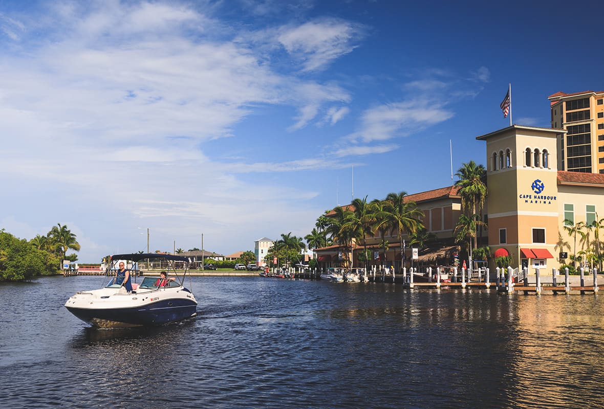 Motorboat cruising a canal past the docks and waterfront buildings at Cape Harbour Marina, Cape Coral.