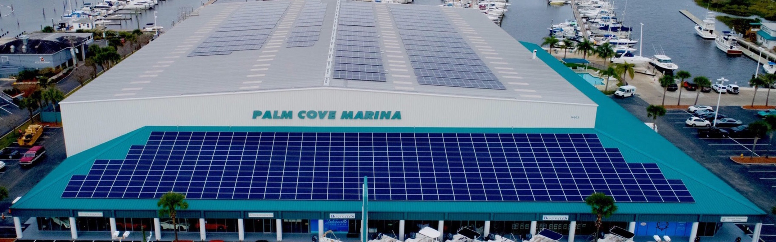 Aerial view of Palm Cove Marina with rooftop solar panels, docked boats and boat sales storefronts, Jacksonville.